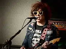 A man with yellow sunglasses singing and playing guitar.
