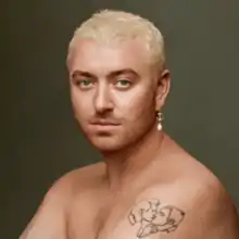 Portrait of Smith with bleached hair, a shoulder tattoo of two men kissing and wearing a golden earring