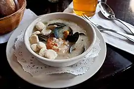 A cream-style seafood chowder at a restaurant, served with oyster crackers in the bowl at left