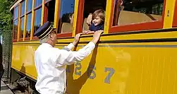 A volunteer conductor greets a child riding in a trolley