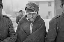 Soviet prisoners of war keep warm with their new clothes. The prisoner in the middle of the photo is staring at the ground with hollow eyes.