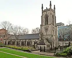 A substantial stone church seen from the north-west. The tower has crocketted pinnacles, and the north wall of the body of the church has a series of large rectangular windows