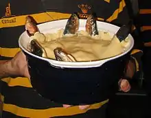 A blue ceramic dish containing a stargazy pie, with six fish poking out of a shortcrust pastry lid, looking upwards