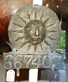 A metal plaque with a sun in the middle and numbers 667403