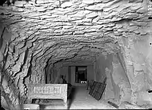 A roughly-cut rock corridor with a bed placed against the left wall