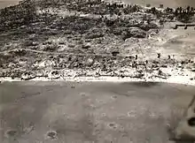 Aerial view of Betio, Tarawa Atoll, 24 November 1943, looking north toward "The Pocket", the last place of Japanese resistance. An emplacement just onshore with two 12.7&nbsp;mm anti-aircraft guns is visible near the left edge of the photograph.