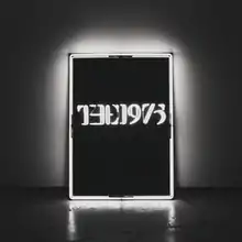 A black-and-white photo showcasing a rectangular, glowing neon sign against a wall in the near-center saying "The 1975".