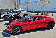 A futuristic-looking ATV between the Tesla Cybertruck and a sports car, the Tesla Roadster (2nd gen.) in a parking lot on the 2020 Tesla Battery Day Event.