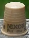 An off-white thimble, with the visible black lettering, "NIXON/Put the ne ...