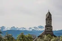 The tower of a church and snowy mountains in the distance