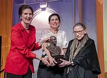 Three women gripping a bust and smiling