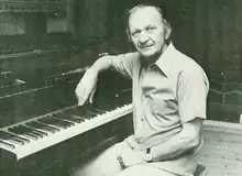 A Caucasian man rests his arm on a piano