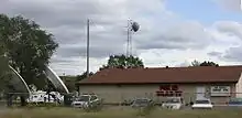 A tan, shed-like building with a red Fox 25 W L A X - T V sign and a small tower with antennas adjacent to it, as seen from a nearby highway