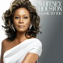 From left to right, the background fades from white to teal. In the foreground, slightly off-center stands an African-American woman in a white over-one shoulder dress. She is smiling and her long hair is flowing. In the right hand corner is her the name of the artist, Whitney Houston followed by the title of the album, I Look to You in a simple white font.