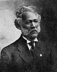 Black and white portrait of a man, wearing suit, with a white collared shirt and a black necktie, with a star on his jacket's lapel.