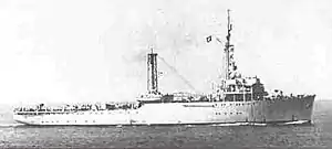 a black and white photograph of a ship at sea with mountains in the background