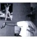 Photo showing military man wearing a t-shirt emblazoned with the phrase 'Women are Property'. On the wall is a poster of a woman in a thong-style undergarment or swimming suit.