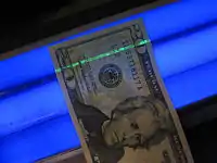 The security thread of a US $20 bill glows green under black light as a safeguard against counterfeiting.
